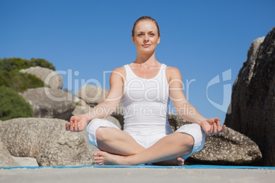 Blonde woman sitting in lotus pose on beach on mat