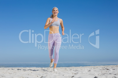 Sporty blonde on the beach jogging towards camera