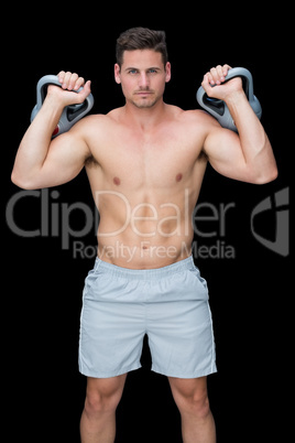 Focused bodybuilder lifting up kettlebells looking at camera