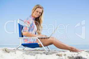 Pretty blonde sitting on beach using her laptop