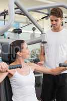 Fit brunette using weights machine for arms with trainer helping