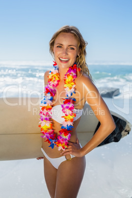 Smiling blonde surfer in white bikini and garland on the beach