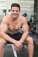 Handsome smiling bodybuilder sitting on bench in weights room