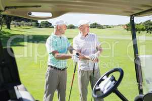 Golfing friends standing beside their buggy looking around