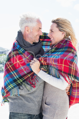 Happy couple wrapped up in blanket standing on the beach