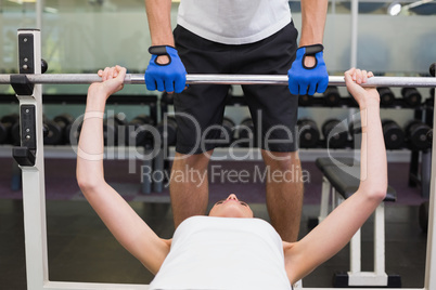 Fit woman lifting barbell with her trainer spotting