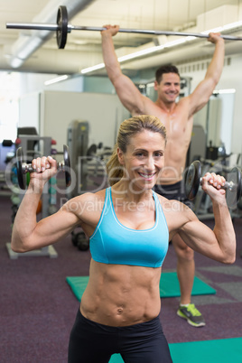 Happy muscular man and woman lifting weights