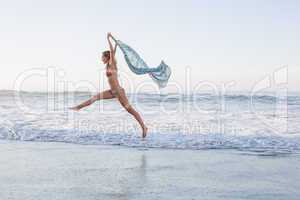 Happy blonde leaping on the beach in bikini with a scarf