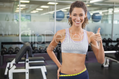 Fit woman measuring her waist and showing thumb up