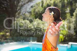 Brunette in sarong smiling by the pool with arms outstretched