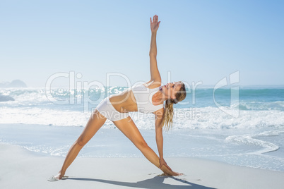 Gorgeous blonde standing in extended triangle pose by the sea