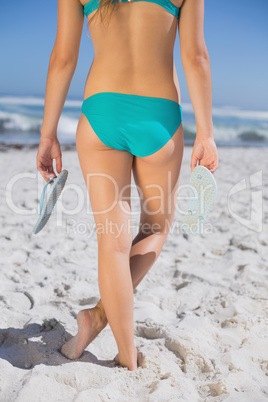 Rear view of fit woman in bikini on beach holding flip flops