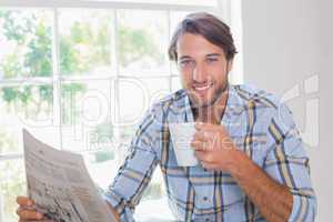 Casual smiling man having coffee while reading newspaper