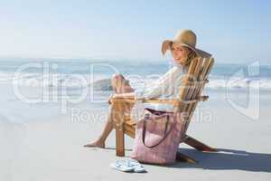 Smiling blonde sitting on wooden deck chair by the sea