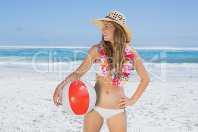 Fit smiling blonde in white bikini and straw hat holding beach b