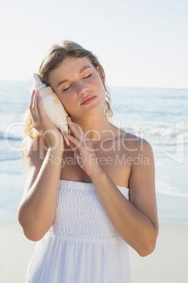 Beautiful blonde in white sundress on the beach listening to con