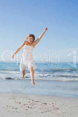 Beautiful blonde in white sundress jumping up on the beach