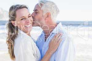Man kissing his smiling partner on the cheek at the beach