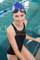 Fit swimmer smiling at camera getting out of the swimming pool