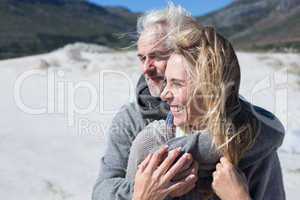 Carefree couple hugging on the beach in warm clothing
