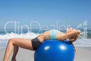 Fit woman lying on exercise ball at the beach stretching