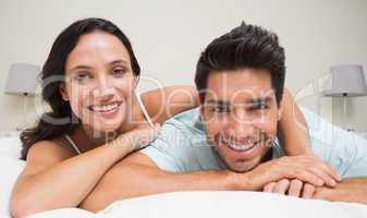 Attractive couple lying on bed smiling at camera