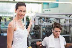 Fit man using weights machine with trainer smiling at camera