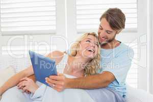 Smiling casual couple sitting on couch under blanket using table