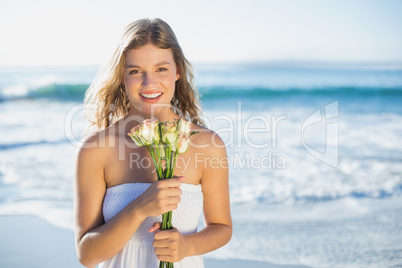 Beautiful blonde in sundress holding roses on the beach