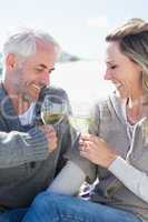 Couple enjoying white wine on picnic at the beach smiling at eac