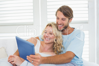 Smiling casual couple sitting on couch under blanket using table