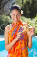 Smiling brunette in sarong showing starfish to camera