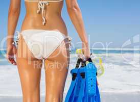 Fit woman in white bikini holding snorkeling gear on the beach