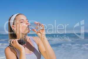Sporty blonde standing on the beach with bottle and skipping rop