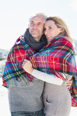 Happy couple wrapped up in blanket standing on the beach