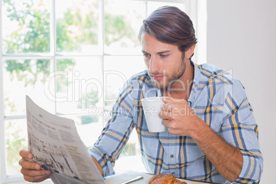 Casual man having coffee while reading newspaper