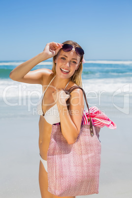 Smiling blonde carrying bag and towel on the beach