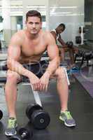Handsome bodybuilder sitting on bench in weights room