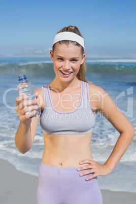 Sporty smiling blonde showing water bottle on the beach