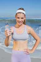 Sporty smiling blonde showing water bottle on the beach