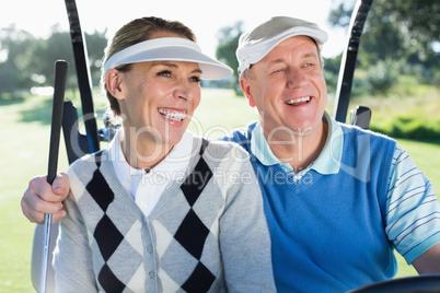 Happy golfing couple sitting in golf buggy smiling