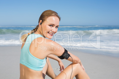 Fit woman sitting on the beach taking a break smiling at camera