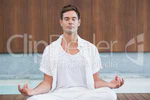 Handsome man in white meditating in lotus pose