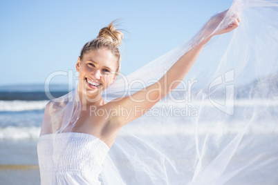 Pretty blonde in white dress holding up shawl on the beach