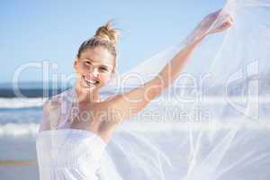 Pretty blonde in white dress holding up shawl on the beach