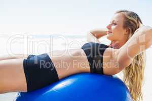 Fit blonde doing sit ups on exercise ball at the beach