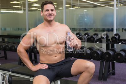 Shirtless bodybuilder sitting on bench with water bottle