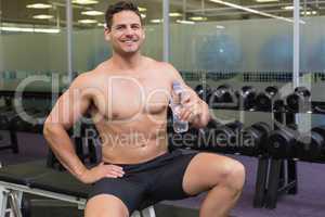 Shirtless bodybuilder sitting on bench with water bottle