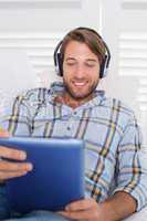 Casual smiling man lying on couch listening to music on tablet p
