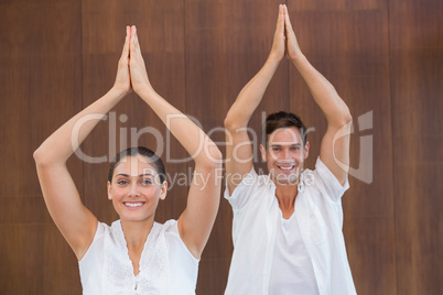 Peaceful couple in white doing yoga together with hands raised